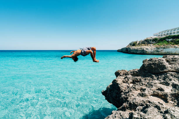 istock Young man is diving in the sea from a cliff doing a backflip 1330224127