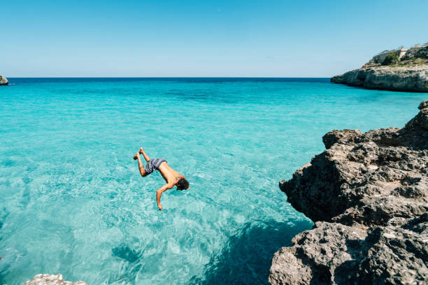 istock Young man is diving in the sea from a cliff doing a backflip 1330224171