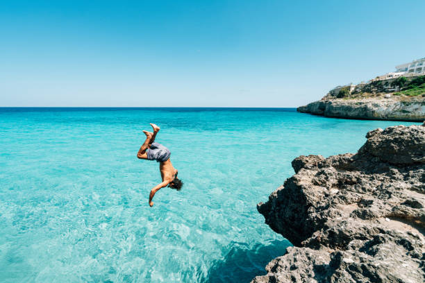 istock Young man is diving in the sea from a cliff doing a backflip 1330224173