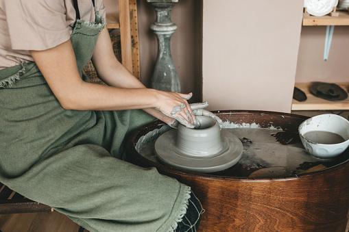 Female ceramics maker or potter working with pottery wheel in workshop. Creative people and handcraft pottery class concept.