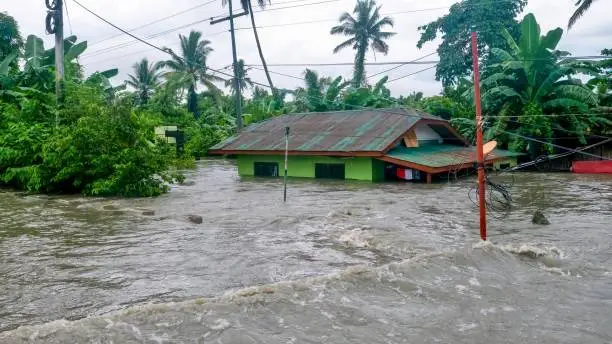 A rural house is nearly submerged by deep floodwater rushing off the National Highway between Baco and Calapan City in Oriental Mindoro province on July 23, 2021. The water level has been rising and now only the upper windows and rooftop are above the water. Conceptual for climate change issues.