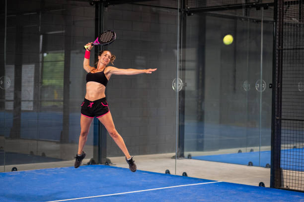 woman playing padel in a blue grass padel court indoor - young sporty woman padel player hitting ball with a racket - padel stockfoto's en -beelden