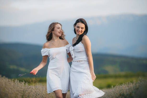 A heartwarming scene of a mother and daughter walking hand in hand through a serene field near a tranquil lakeside during the golden hour of the evening. The soft, warm light of the setting sun casts a peaceful glow over the landscape. The mother and daughter share a quiet moment, enjoying the beauty of nature as they stroll through the tall grass, creating a sense of connection and tranquility.