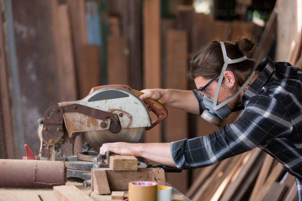 istock Male carpenter wearing safety dust filter mask at work. woodworker using circular saw cutting piece of wood at woodwork workshop 1330236748