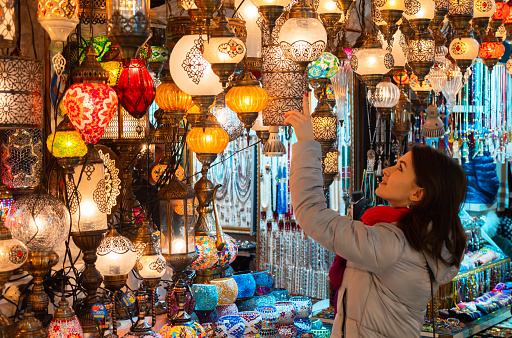 Young woman touching Turkish lamps for sale in the Grand Bazaar, Istanbul, Turkey