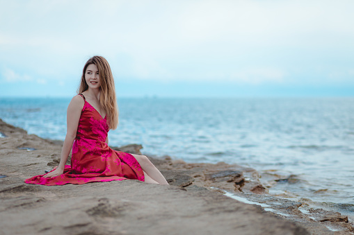 Young woman in a pink dress sitting on the beach
