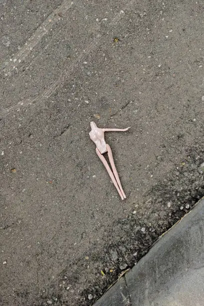 Broken doll without a head and one arm lying on an asphalt road