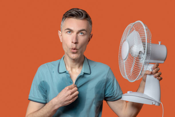 istock Man in tshirt with wet spots with fan 1330244999