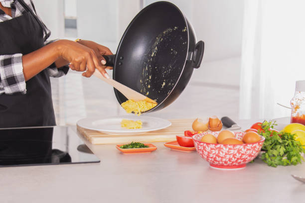 istock Scrambled eggs being poured from a deep frying pan into a plate 1330247354