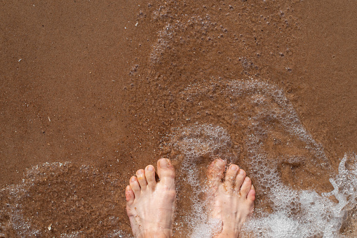 Looking at a mans feet covered in black dirt standing on white sand