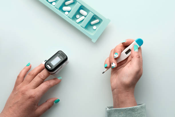 istock Patient hands with pills and pulse oximeter, finger digital device to measure oxygen saturation in lungs. Mature caucasian female hand. Reduced oxygenation is sign of pneumonia, covid illness 1330251619