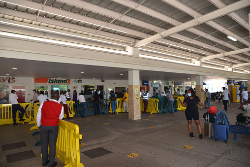 Montego Bay, Jamaica - May 18,2021 : Passengers and skycaps gathered at the entrance to the Montego Bay airport waiting on taxis, shuttle services and car rentals to start their vacation on an early springtime day in Jamaica