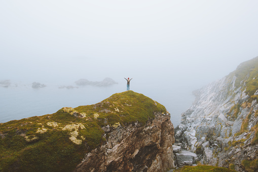 Woman standing alone on rocky cliff  travel vacation adventure lifestyle outdoor raised hands isolation solitude concept foggy seaside landscape in Norway