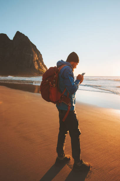 Traveler man with using smartphone on Kvalvika beach navigation technology influencer blogger lifestyle summer vacations outdoor sunset ocean view
