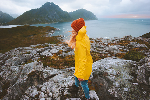 Tourist woman walking in Norway mountains vacations outdoor adventure lifestyle girl wearing yellow raincoat explore Lofoten islands