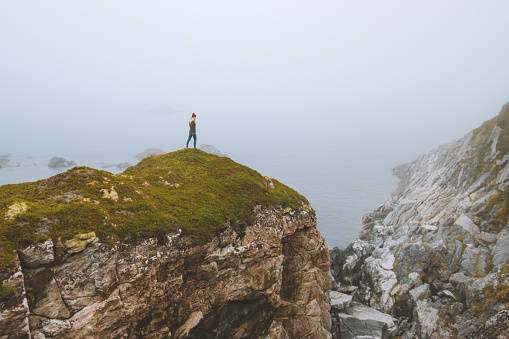 Solo travel woman standing alone on rocky cliff vacation adventure lifestyle outdoor isolation solitude concept foggy seaside landscape in Norway