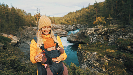 Mother walking with baby carrier in forest family traveling in Norway vacation  outdoor woman with infant child together healthy lifestyle autumn season
