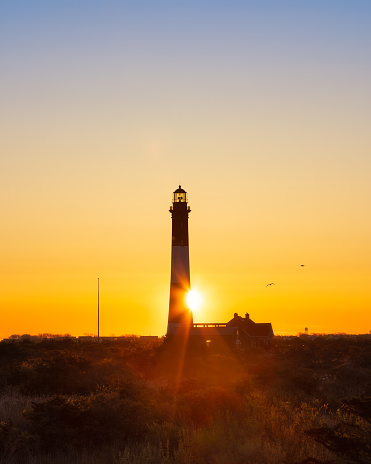 Sun rising from behind a tall lighthouse, creating a golden star burst. Fire Island, Long Island New York