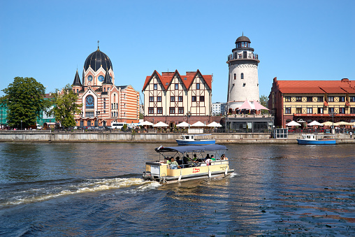 Kaliningrad, Russia - June 18, 2021. Fishing Village on the embankment Pregolya river. Tourist center of the city with lighthouse, walking paths, pleasure boat and cafes. Stylized architecture of pre-war Konigsberg  buildings in the German style