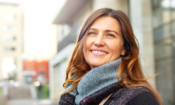 Attractive adult smiling woman against the backdrop of city buildings. Portrait of a successful woman with a beautiful smile and eyes in a warm sweater and sun glare. mock turtleneck stock pictures, royalty-free photos & images