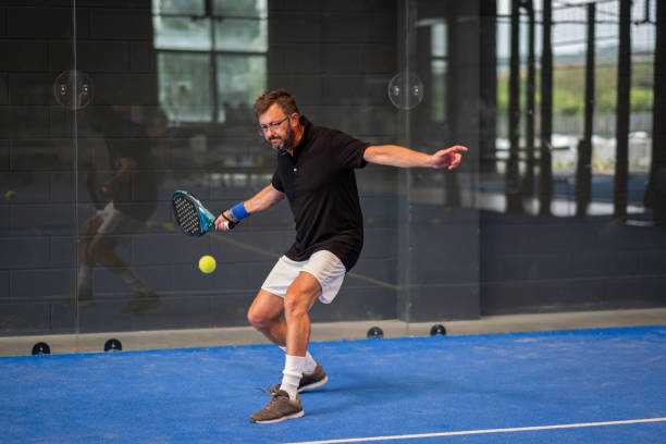 man playing padel in a blue grass padel court indoor - young sporty boy padel player hitting ball with a racket - padel imagens e fotografias de stock
