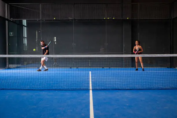 Mixed padel match in a blue grass padel court indoor behind the net
