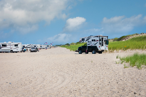 Barnstable, Massachusetts, USA- July 22, 2021-  A truck camper slowly drives over the soft deep sand of Sandy Neck Beach on Cape Cod as he tries to find a parking spot overlooking the ocean.