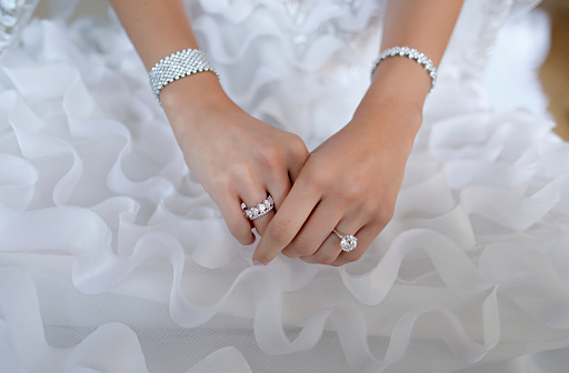 Bride's hand with beautiful diamond ring and jewelry on white dress