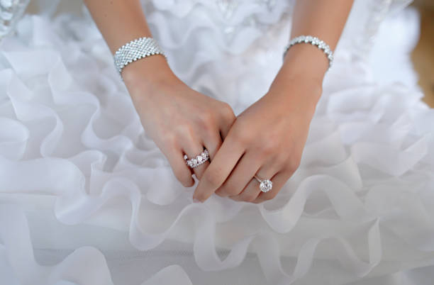 Bride's hand with beautiful diamond ring and jewelry on white dress Bride's hand with beautiful diamond ring and jewelry on white dress diamond ring stock pictures, royalty-free photos & images