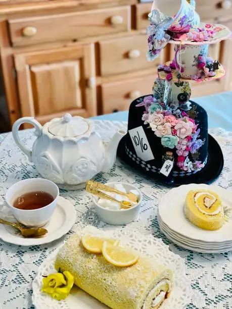 Beautiful table setting, ornate vintage tea set. Floral arrangement, teapot, full teacup, light delicious lemon flavored cake roll. Themed tea party.