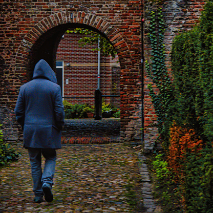 Amersfoort, Netherlands - October 25 2020 : a mysterious looking  hooded man is walking in the evening towards the entrance gate of an historic medieval dutch city passing over a stone brick bridge