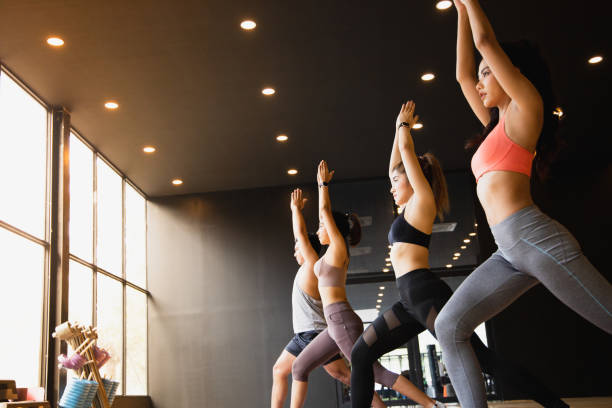 un grupo de jóvenes asiáticos que están en buena forma estudiando yoga con un entrenador están en una pose de guerrero 1. - centro de yoga fotografías e imágenes de stock