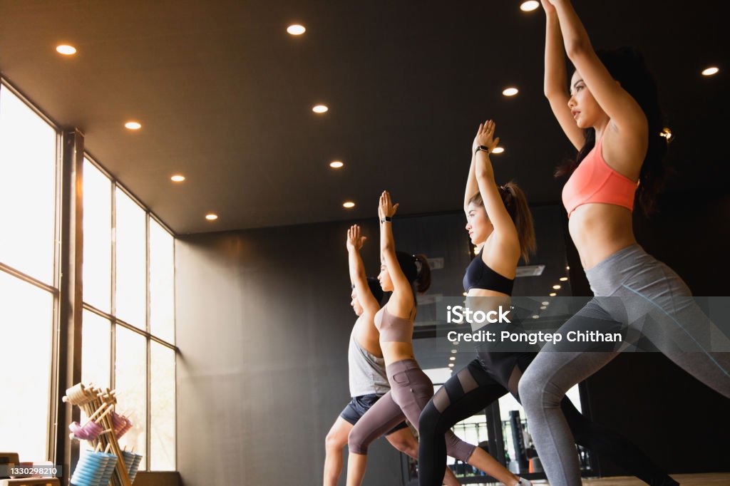 A group of young Asian people who are in good shape studying yoga with a trainer They are in a warrior 1 pose. Pilates Stock Photo