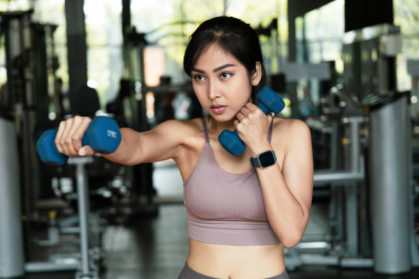 An Asian women Exercise with dumbbells for boxing in fitness gym.  With a boxing dumbbell workout boxers will develop the muscles in arms. self care and Lose weight concept stock photo
