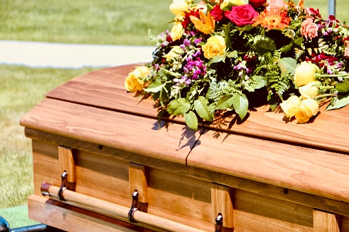 Beautiful floral arrangement on wooden casket at graveside service in cemetery