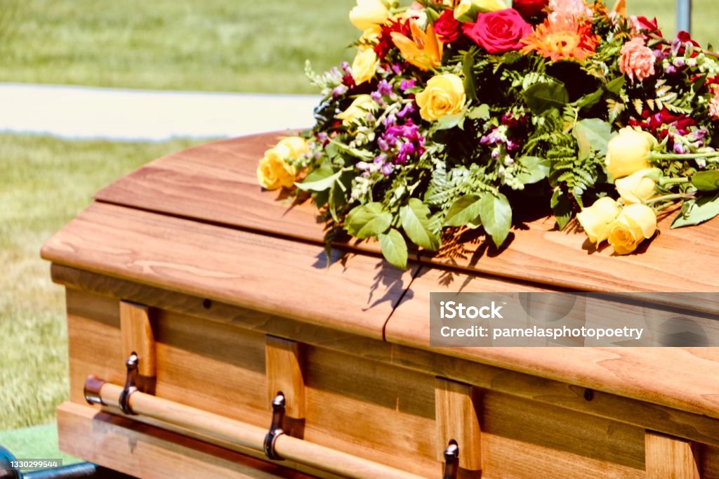 Floral arrangement on casket at graveside Beautiful floral arrangement on wooden casket at graveside service in cemetery Funeral Stock Photo