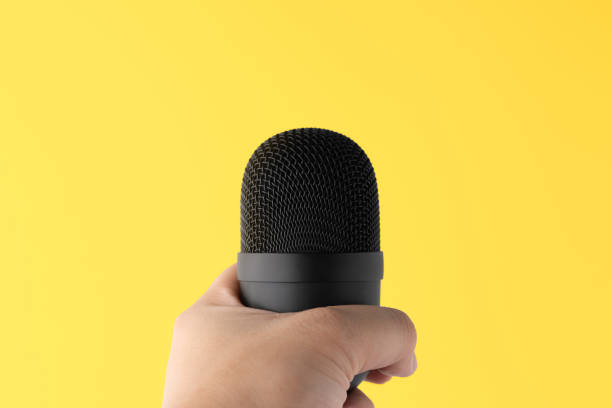 istock Hand holding microphone, yellow background, live video streaming concept. 1330300192