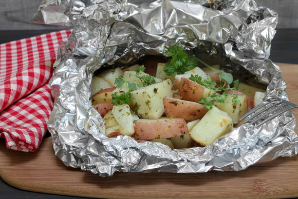 Baked potatoes and one unwrapped with sour cream, herbs and bell pepper.