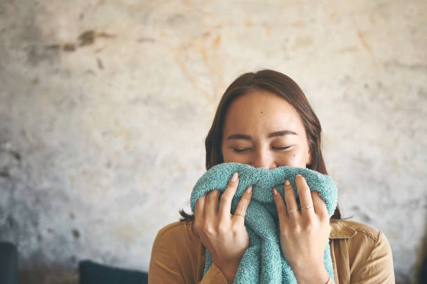 foto de una mujer joven oliendo a ropa recién lavada en casa - oliendo fotografías e imágenes de stock