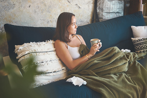 Foto de una mujer joven tomando una bebida caliente mientras se recupera de una enfermedad en el sofá de casa photo