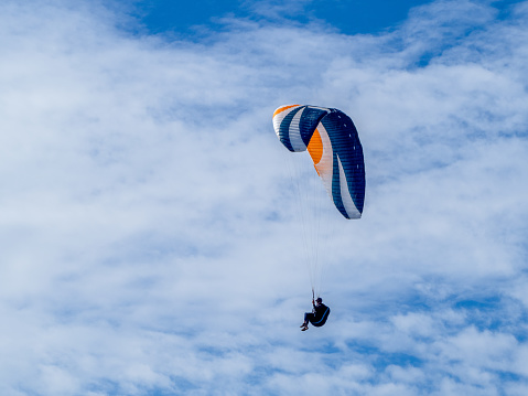 Horizontal landscape photo of a man using a colorful paraglider to float in the sky above the north coast of NSW at Lennox Head near Byron Bay, NSW