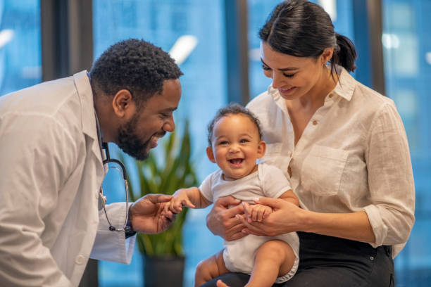 Cute baby at the doctor's office An adorable boy smiles while his mother holds him and a doctor crouches to interact with the baby. 3 6 months stock pictures, royalty-free photos & images