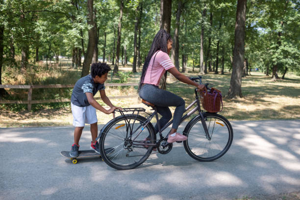 istock Mother Riding Bicycle And Pulling Her Son On Skateboard 1330325271