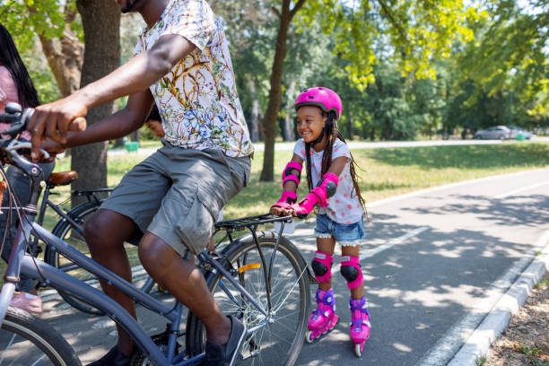 istock Father Riding Bicycle And Pulling His Daughter On Roller Skates 1330325301