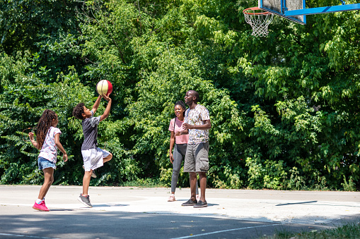 African family with two kids playing basketball outdoors. Boy is throwing the ball.