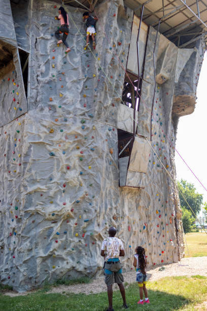 Cute African family spending time together outdoors. Mother and son wall climbing while father and daughter watching.
