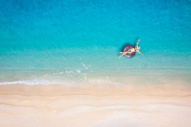 eine frau im bikini schwebt auf einem donutförmigen aufblasbaren über türkisfarbenem, klarem meer - sea swimming greece women stock-fotos und bilder