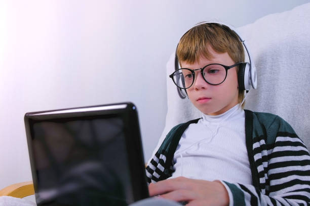 istock Boy in glasses and earphones is writing on laptop. Online study and learning. 1330341634