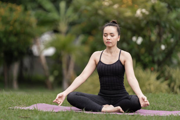 A confident middle-aged Asian woman in sports outfit doing yoga exercise on the yoga mat outdoor in the backyard in the morning. Young woman doing yoga exercise outdoor in nature public park stock photo