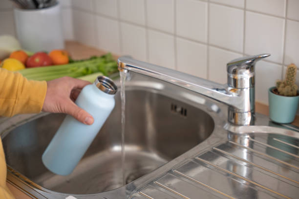 istock Man fills up reusable water bottle in the kitchen 1330353330